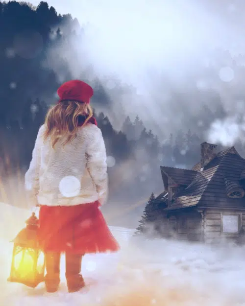 Young girl with lantern stood in the snow looking at a house
