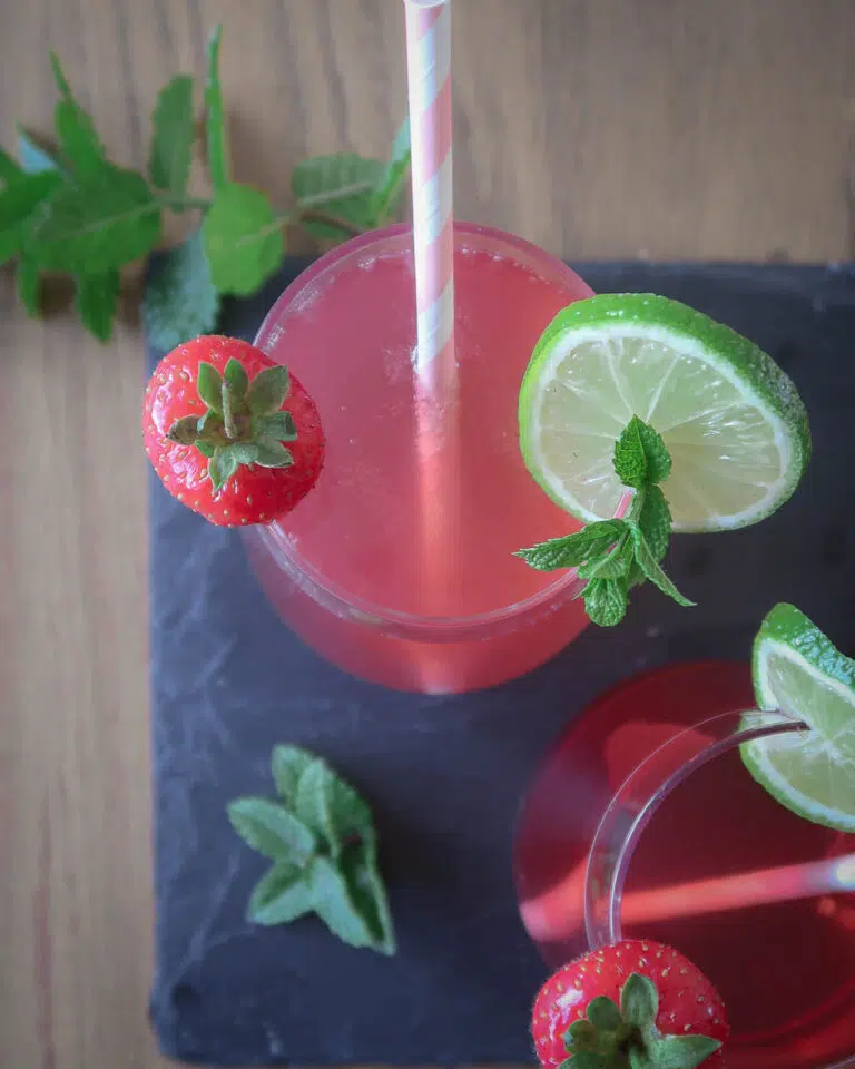 Overhead shot of a pink cocktail with a fresh strawberry, lime and mint garnish.