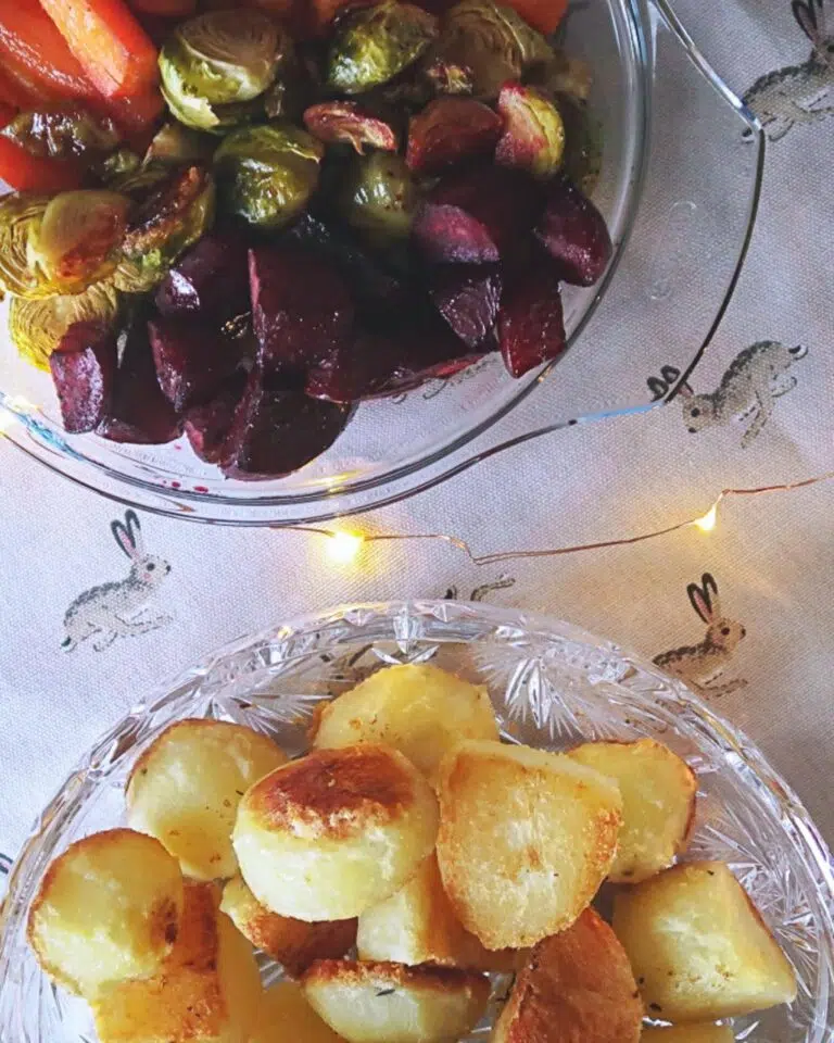 A bowl of crispy roasted potatoes and a trio of roasted vegetables; beetroot, Brussels sprouts and red pepper