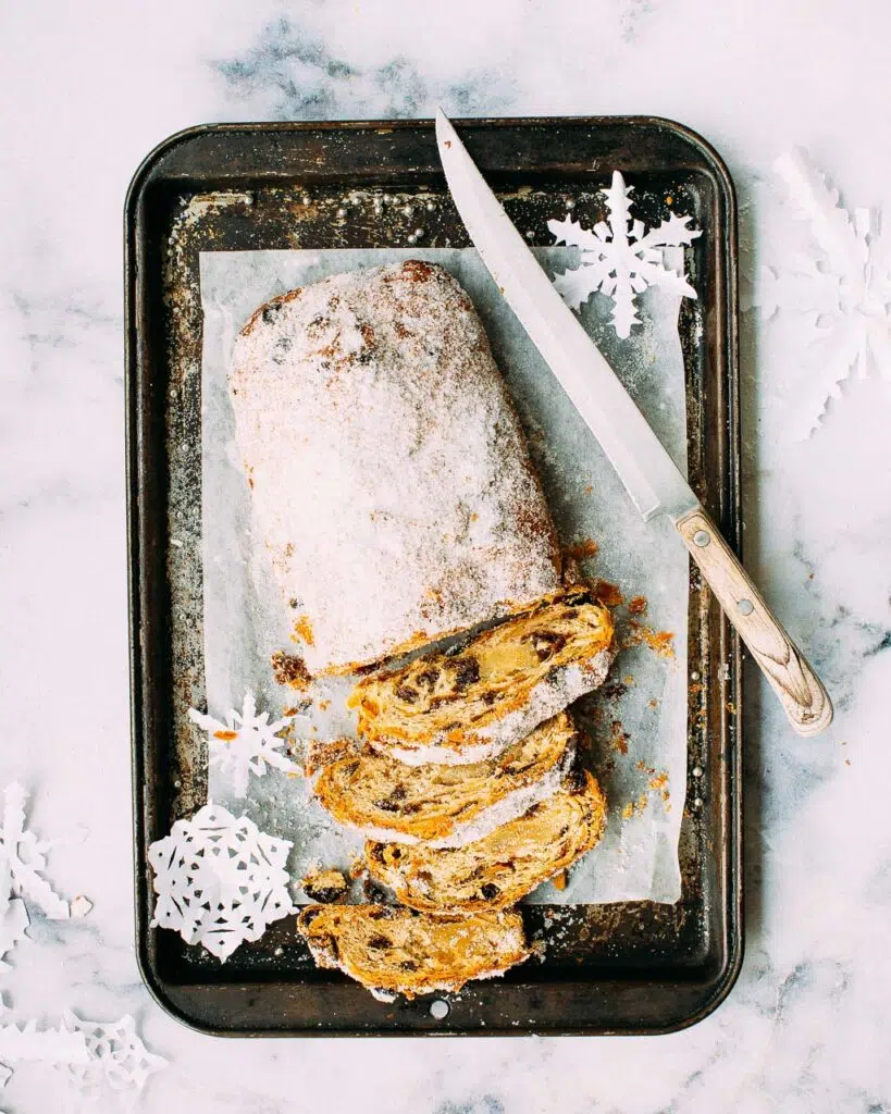 Slices of marzipan filled stollen on a black metal tray, with snowflake decorations