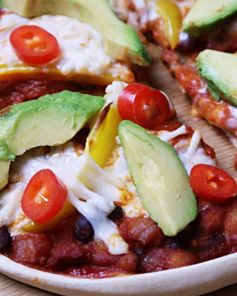 A homemade pizza with vegan bean chilli, vegan cheese, avocado and red chilli