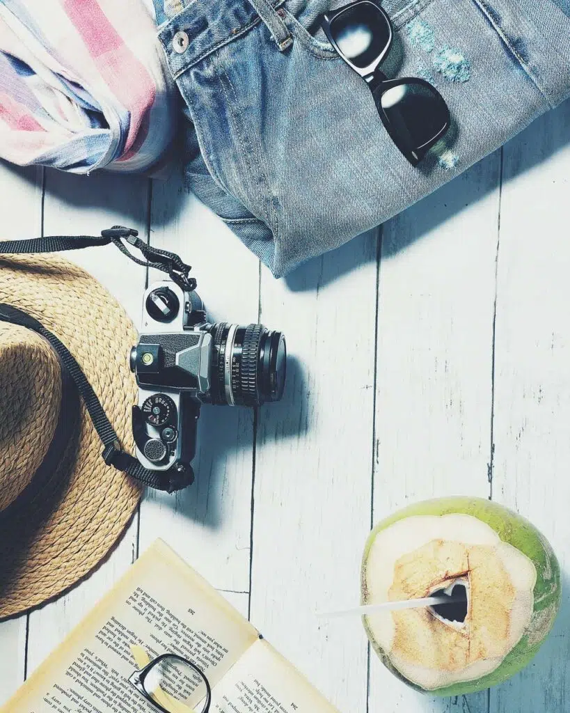 Flat lay with a coconut, camera, straw hat, jean shorts, sunglasses and book