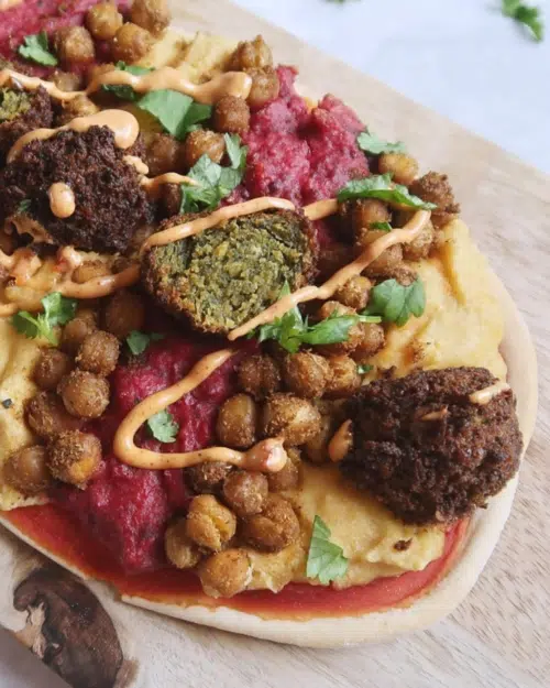 A pizza base with houmous, beetroot houmous, falafel, spiced roasted chickpeas and vegan mayo