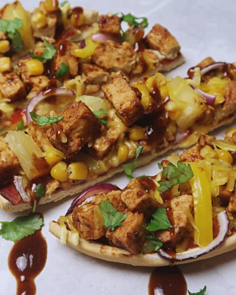 A pizza base with vegan chicken, yellow pepper, jerk sauce, red onion and fresh coriander