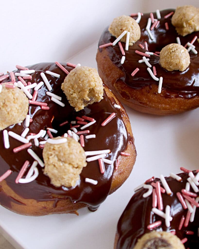 A box of chocolate glazed doughnuts with pink and white sprinkles and mini balls of cookie dough
