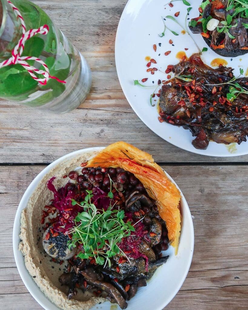 Birds eye shot of two bowls of vegan food with flat bread, mushrooms, vegan cheese and salad