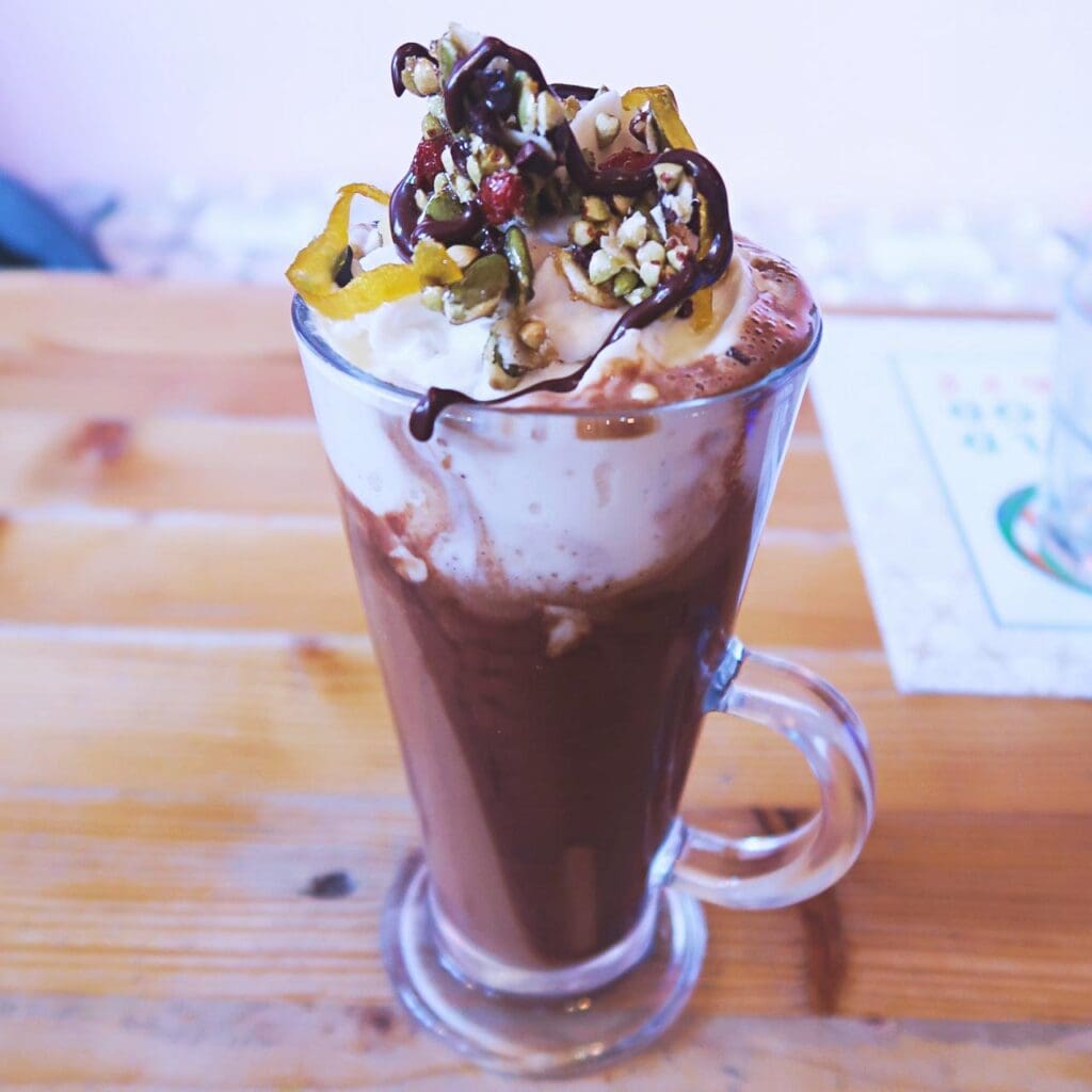 Tall glass of vegan hot chocolate topped with whipped cream, nuts and seeds