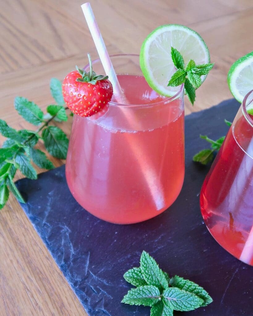 A pink cocktail with a fresh strawberry, lime and mint garnish.
