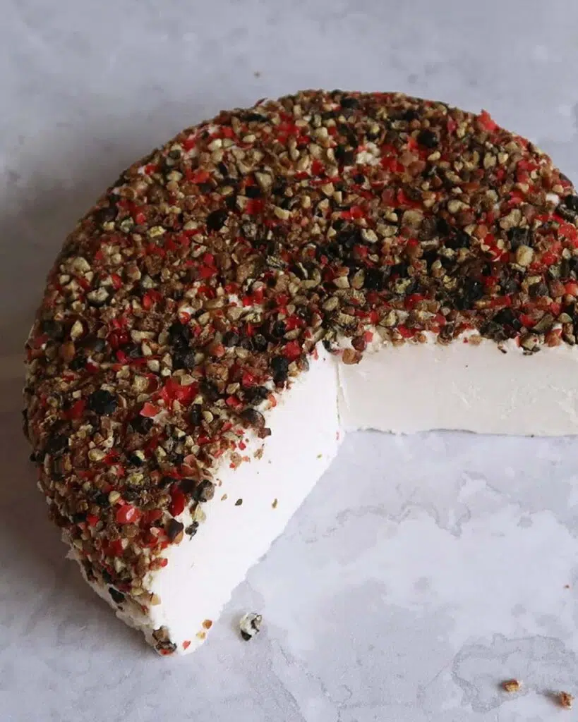 A round of vegan cheese topped with black and red peppercorns