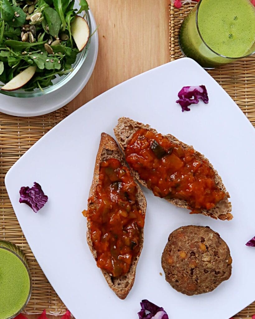 Vegan burger next to ratatouille on toast, an apple salad and fresh green juice