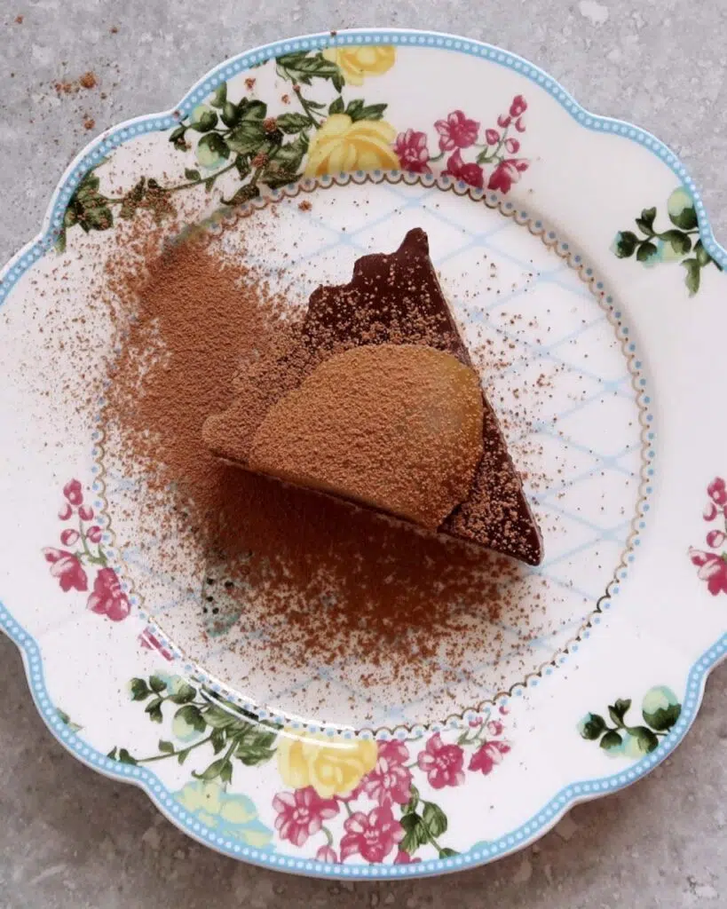 Birds eye view of a vegan chocolate torte with a slice of poached pear on top and a dusting of cocoa powder