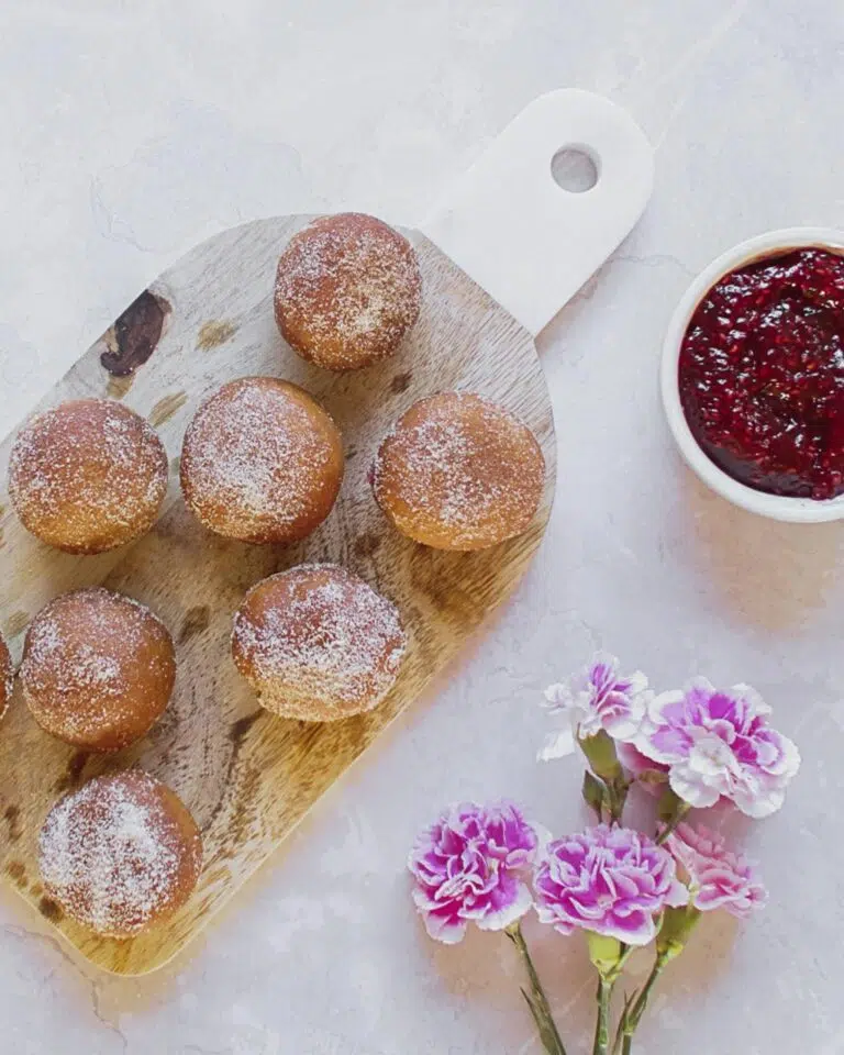 Sugar coated doughnut holes on a wooden board with a pot of raspberry jam beside