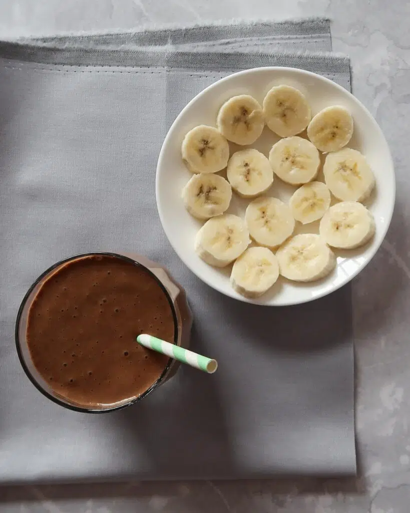 Flatlay of a healthy banana chocolate milkshake and a plate of fresh banana slices