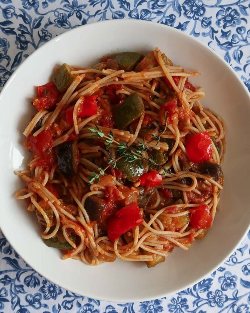 Top down photo fo a bowl of spaghetti with ratatouille vegetables mixed in and a sprig of fresh thyme on top