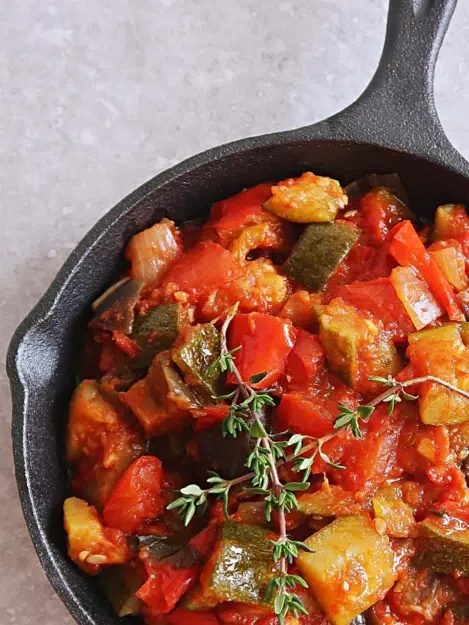 Oven baked ratatouille in a cast iron pan with a sprig of fresh thyme on top