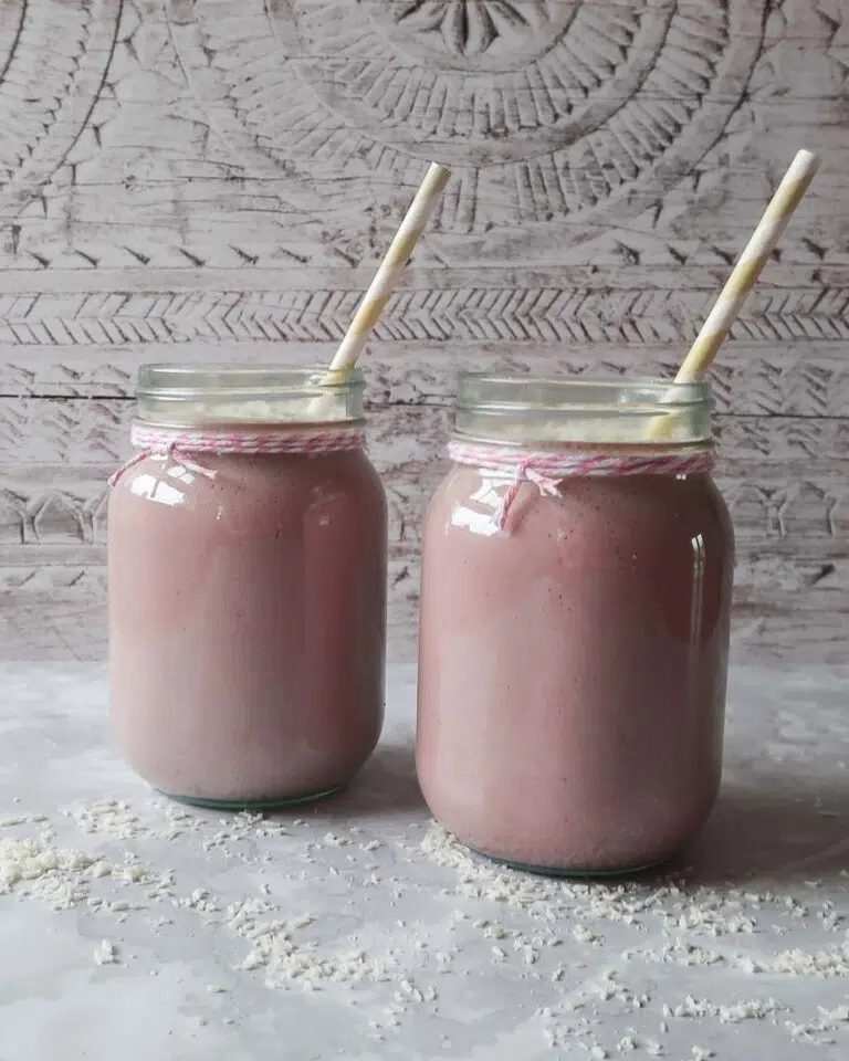Two large jars of vegan strawberry milkshake with a sprinkling of desiccated coconut and yellow striped straws