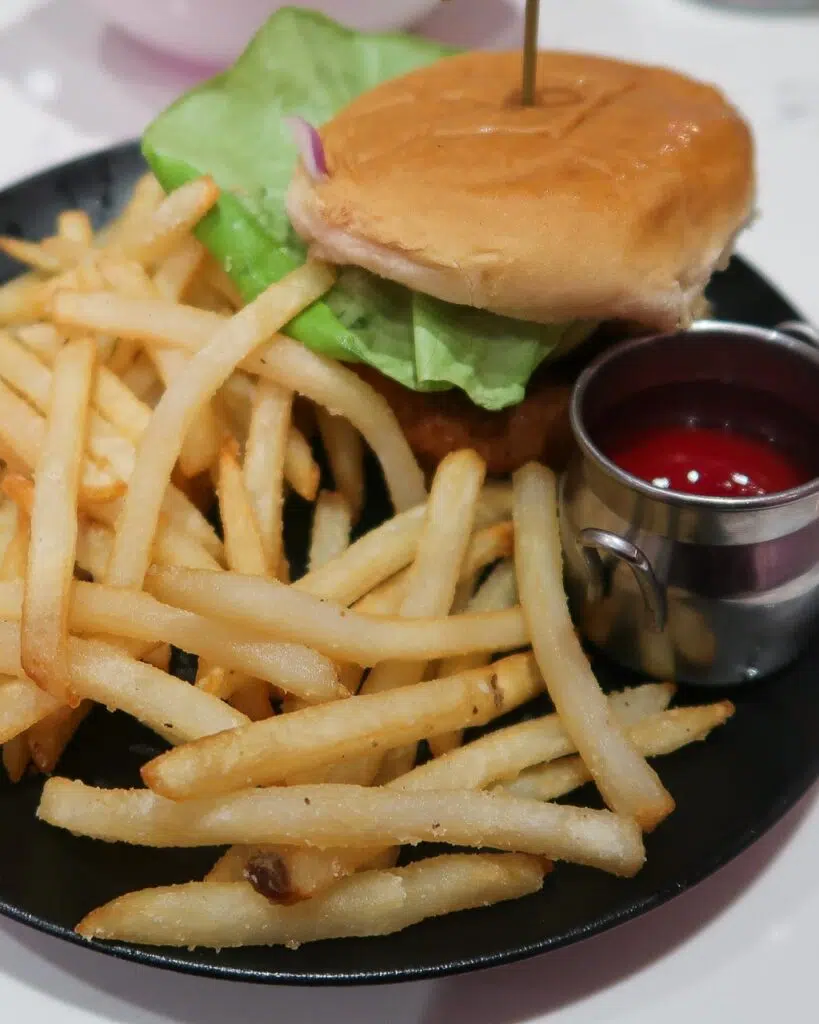 A black plate topped with skinny fries and a beyond burger in a vegan brioche bun with fresh lettuce and a side of ketchup