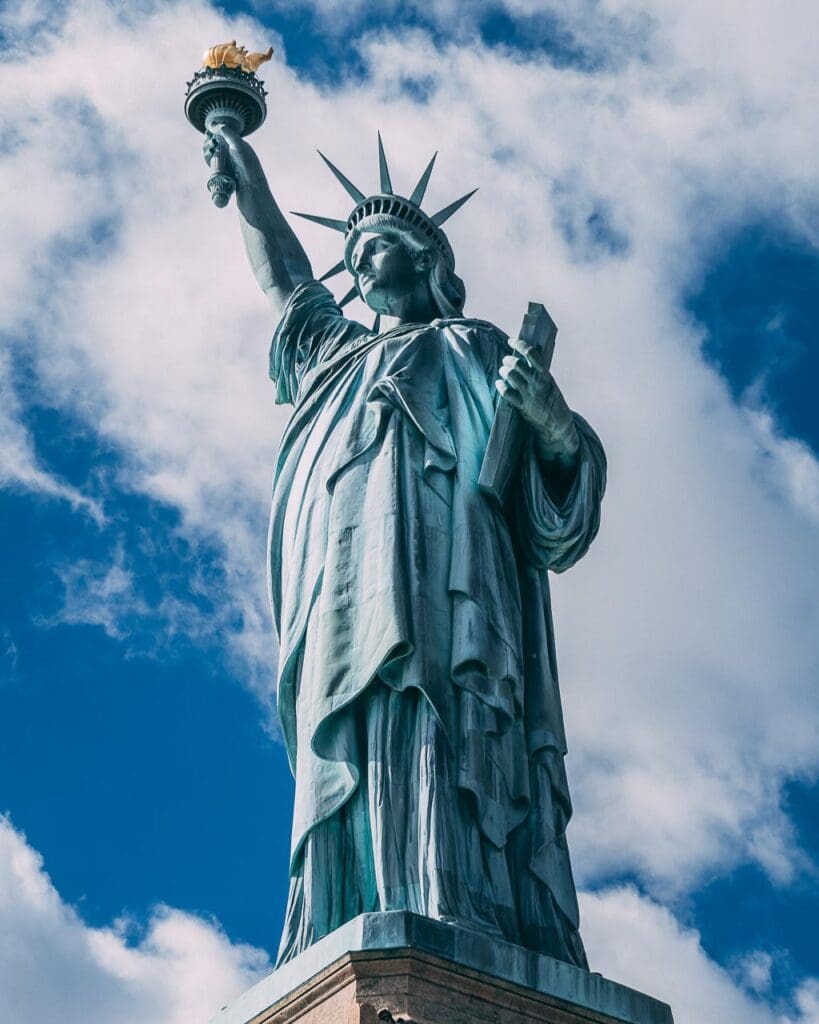 Looking up at the Statue of Liberty with the blue sky and white clouds behind.