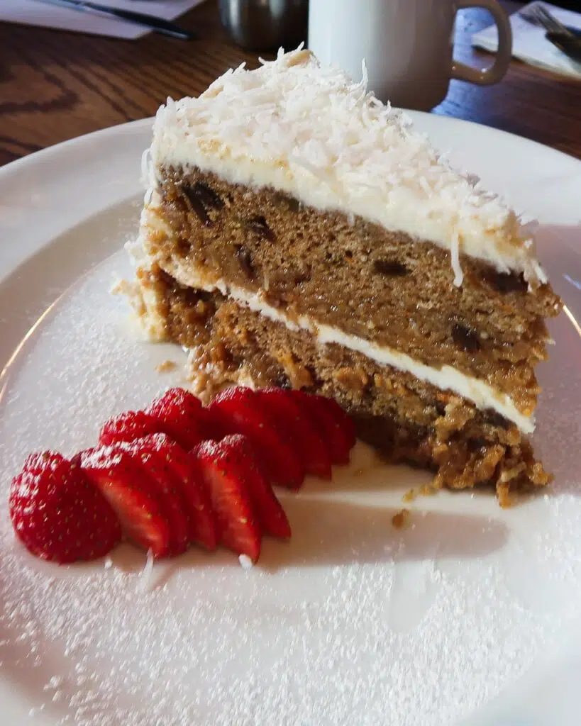 A large slice of vegan carrot cake from Spring Street Naturals served on a white plate with sliced strawberries