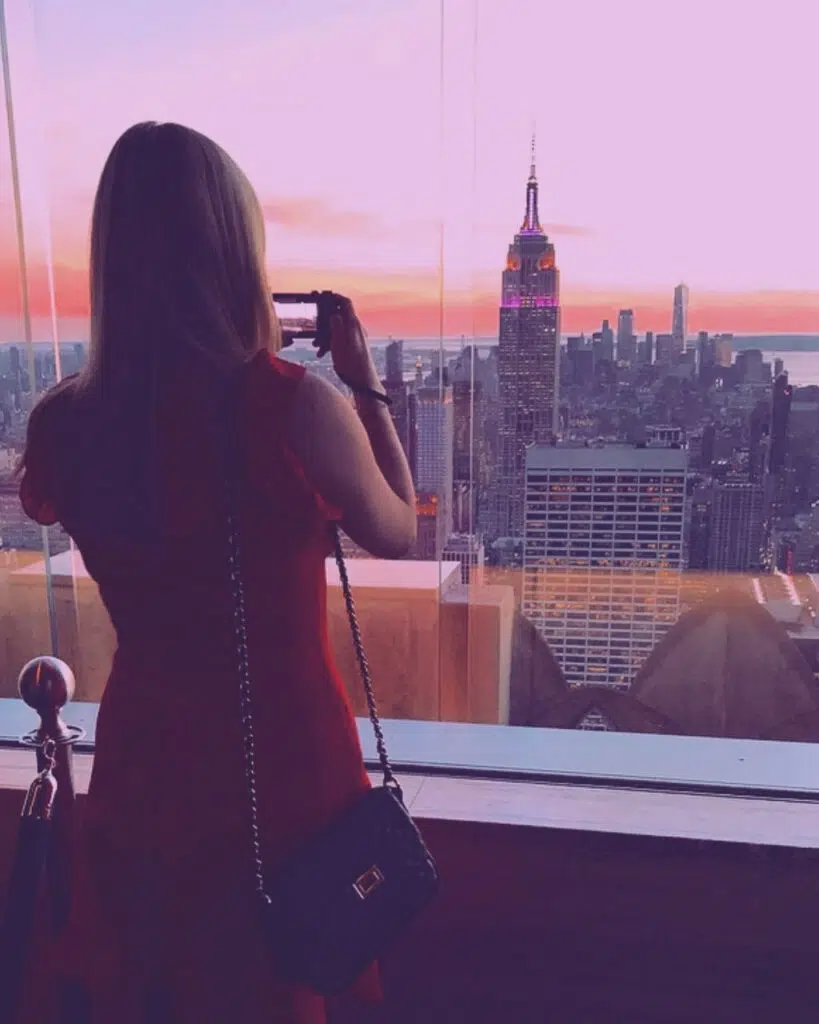 A young woman stood at the window of the Rainbow Room in New York City, overlooking the view of the city at sunset