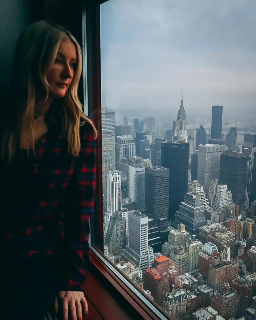 A blonde woman in a check flannel shirt sat in the window of the Empire State Building overlooking the view