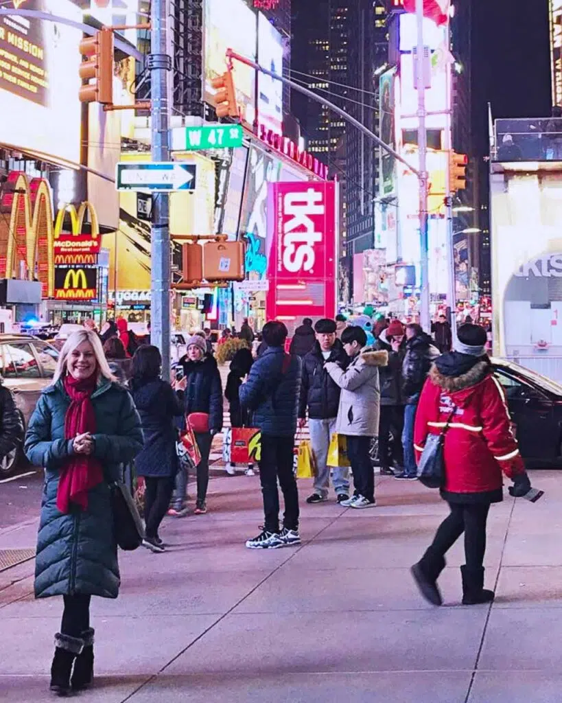 A blonde woman in a black coat and red scarf stood outside in Times Square