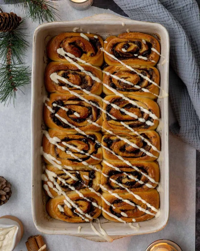 A large rectangular cream dish of 12 squishy cinnamon rolls that have been freshly baked and are topped with a zig zag of white tofu icing.