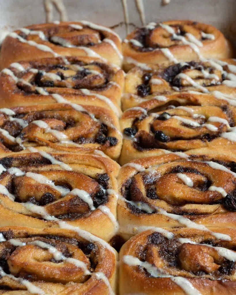 A long row of squishy freshly baked cinnamon rolls with a zig zag of white icing across them