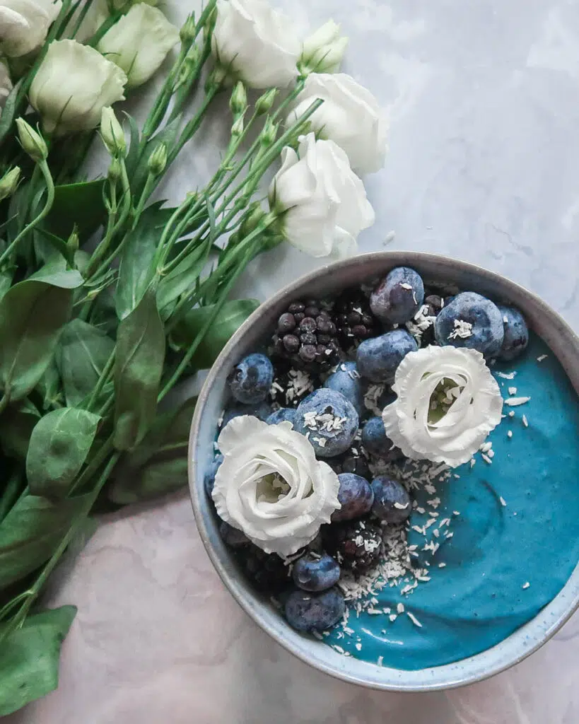 Pretty bright blue smoothie bowl with fresh blueberries, coconut and white flowers