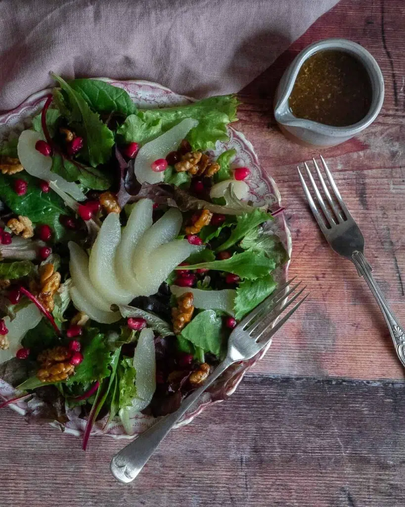 A colourful salad with poached pear slices, pomegranate seeds and candied walnuts on a pink floral plate