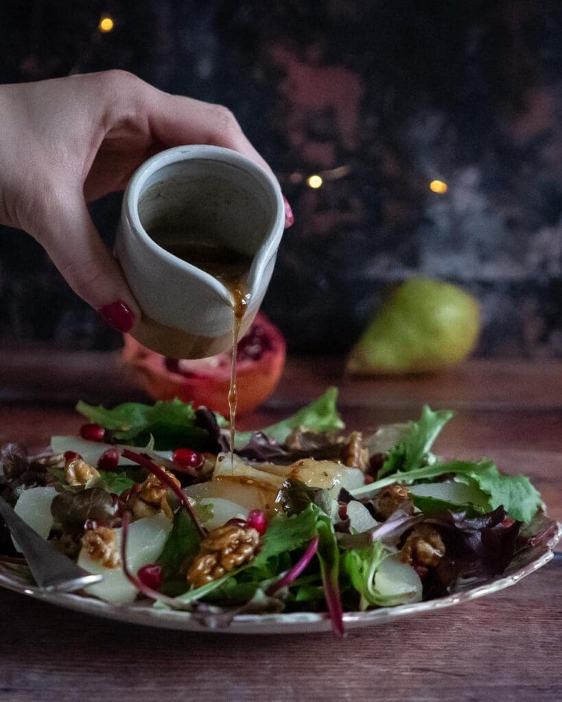 A colourful salad with poached pear slices, pomegranate seeds and candied walnuts on a pink floral plate