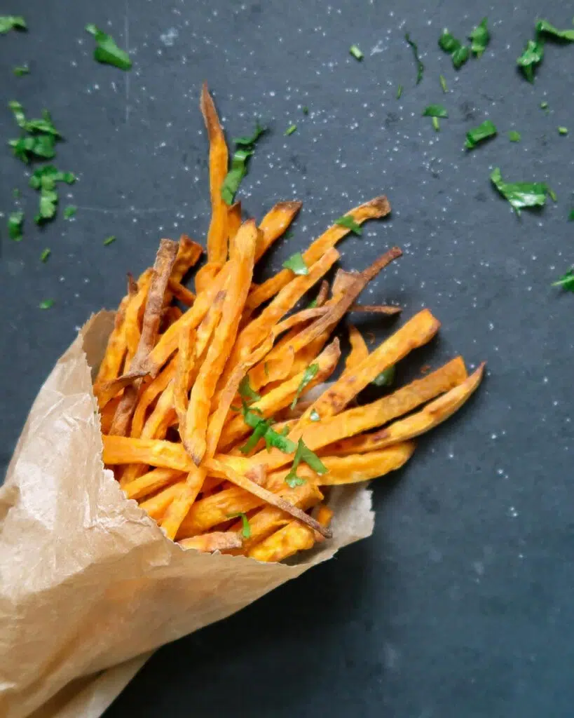 A brown paper bag of skinny sweet potato truffle fries topped with a sprinkling of parsley