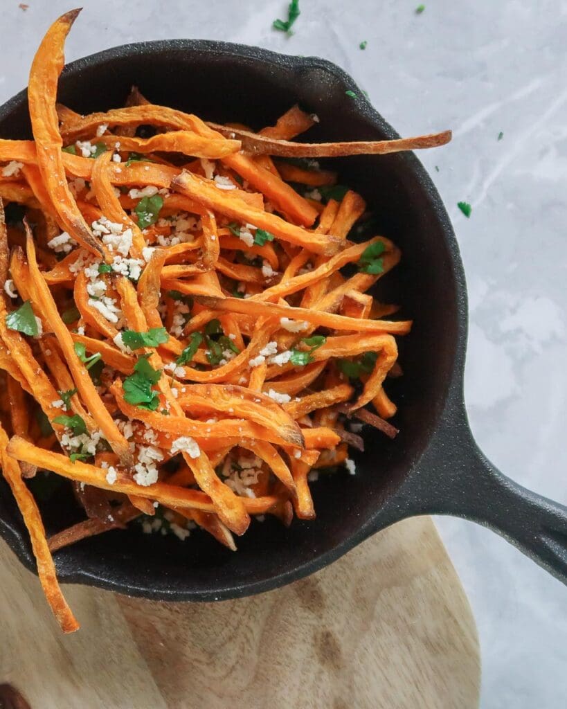 A cast iron pan holding skinny sweet potato truffle fries topped with a sprinkling of vegan parmesan and parsley