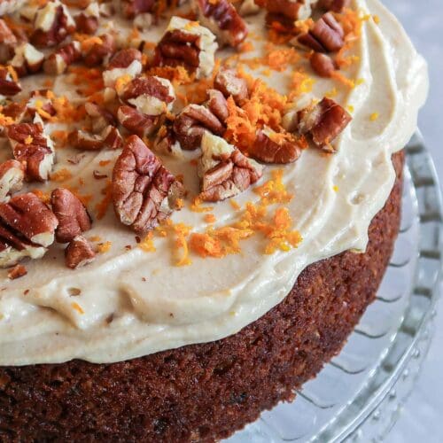 A moist vegan carrot cake topped with fluffy tofu frosting, grated orange zest and pecans