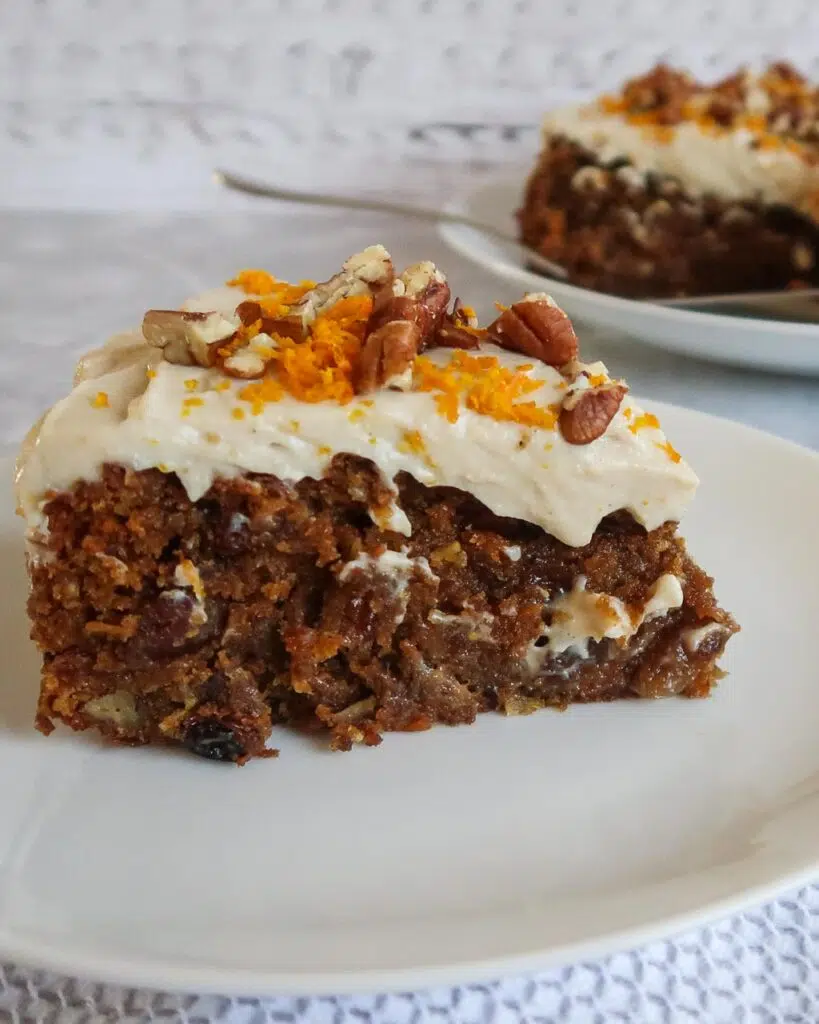A slice of moist vegan carrot cake topped with fluffy tofu frosting, grated orange zest and pecans