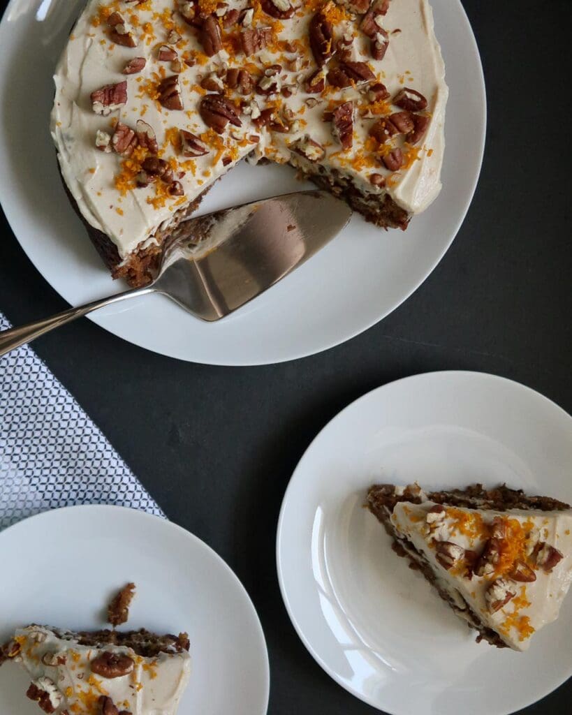A moist vegan carrot cake topped with fluffy tofu frosting, grated orange zest and pecans