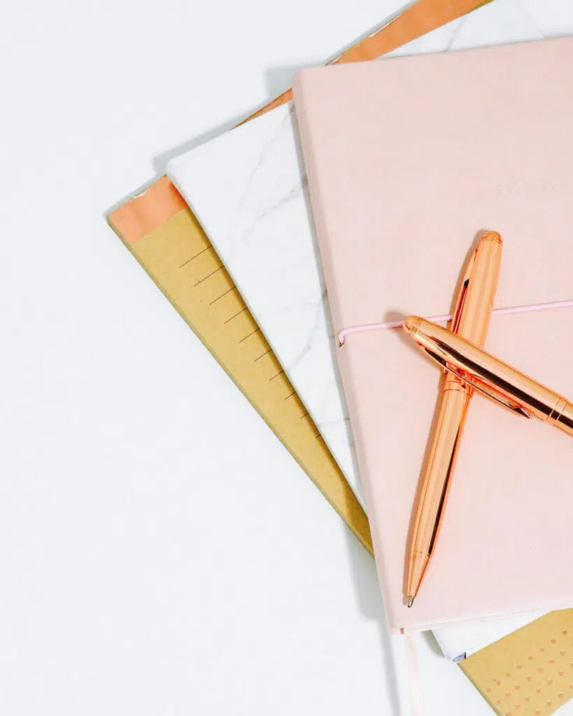 Three notebooks stacked with two rose gold pens on top