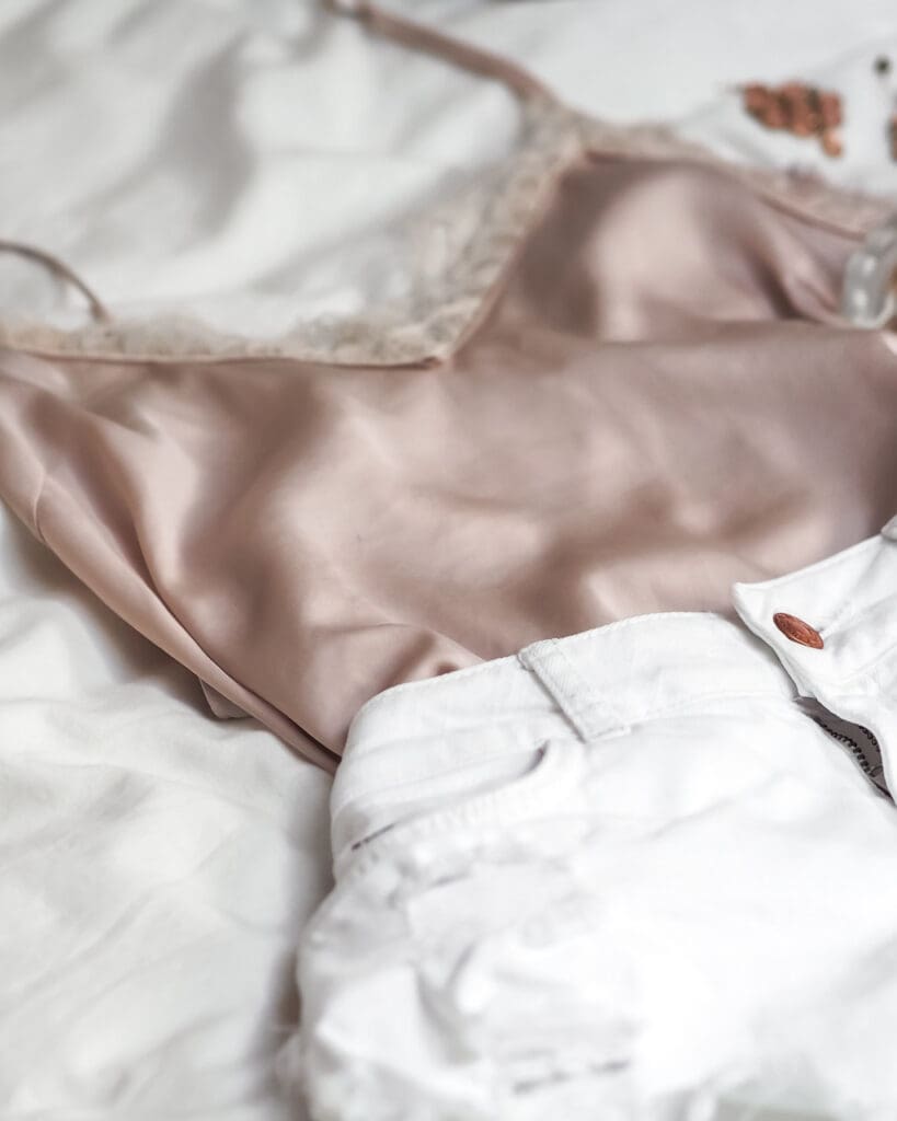 A pink lacy vest and white denim shorts laying on a bed