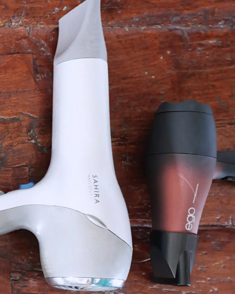 A standard hair dryer laying next to a smaller travel hair dryer