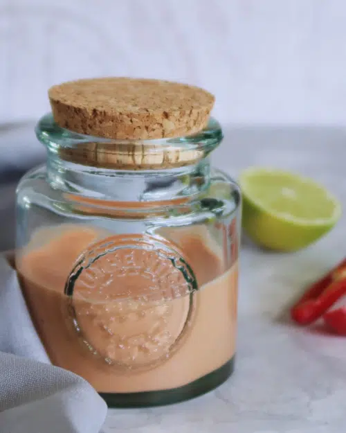 A glass bottle with cork stopper holding a creamy vegan chilli sauce