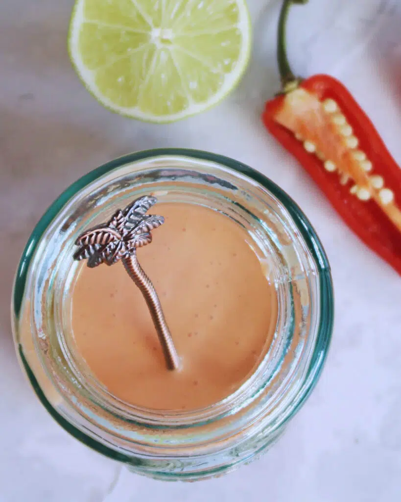 A glass bottle holding a creamy vegan chilli sauce