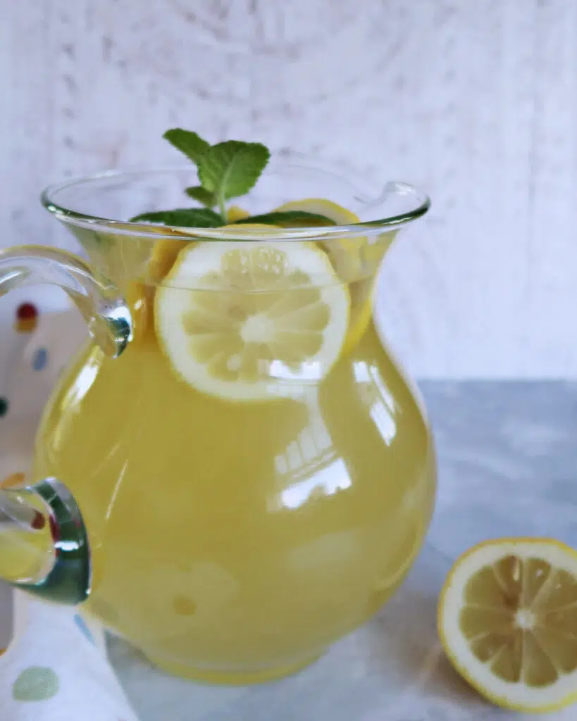 A glass jug of freshly made lemonade with fresh lemon slices and fresh mint on top