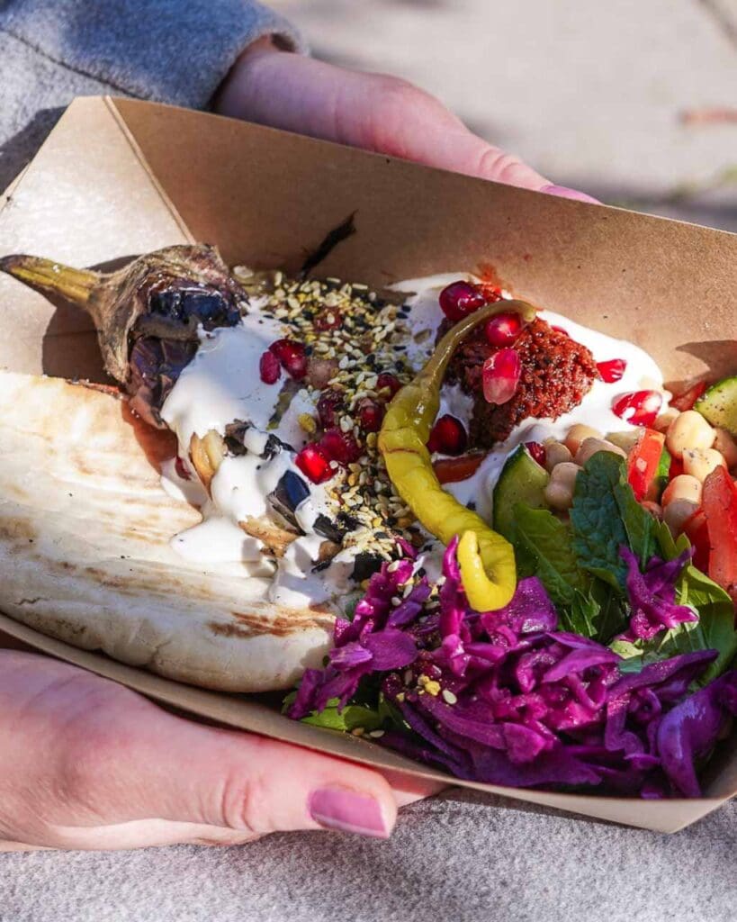 A colourful takeaway dish of fire roasted aubergine with red cabbage, picked jalapeno and flat bread