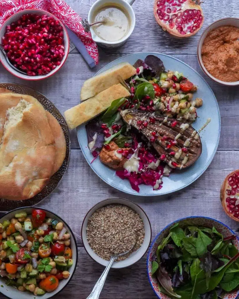 A flatlay of a middle eastern feast with roasted aubergine, pickles, salads and flatbreads.