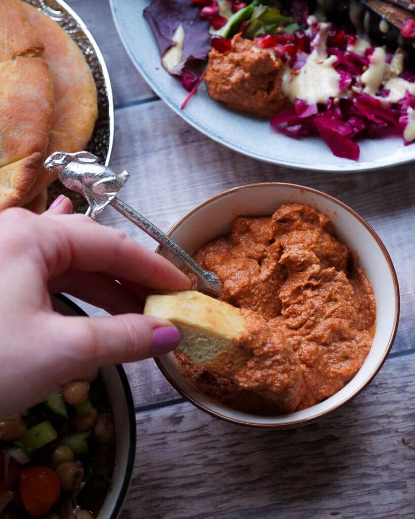 A bowl of roasted red pepper dip with flat bread being dipped in