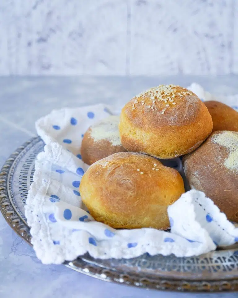 Beautiful orange sweet potato bread rolls on a silver tray lined with a white and blue dot lace napkin