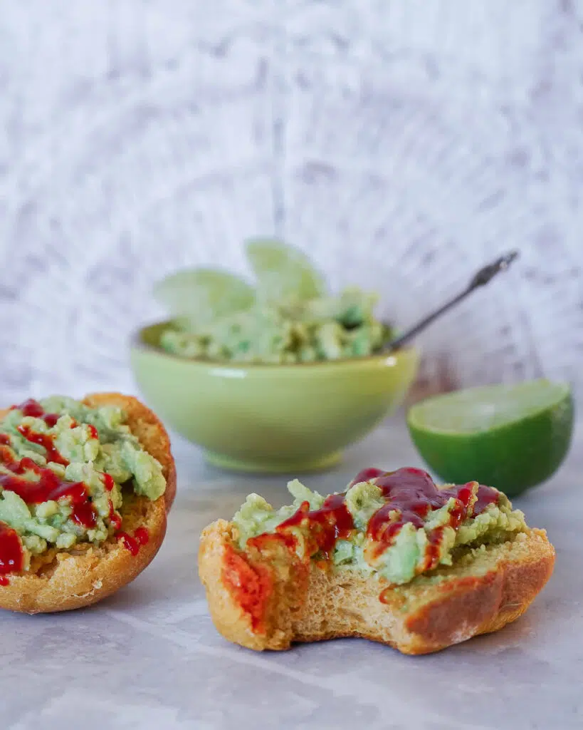 A sweet potato bread roll cut in half with mashed avocado and chilli sauce on top