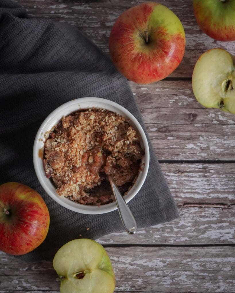 Mini apple crumble pot on a wooden backdrop with fresh green and red apples surrounding it