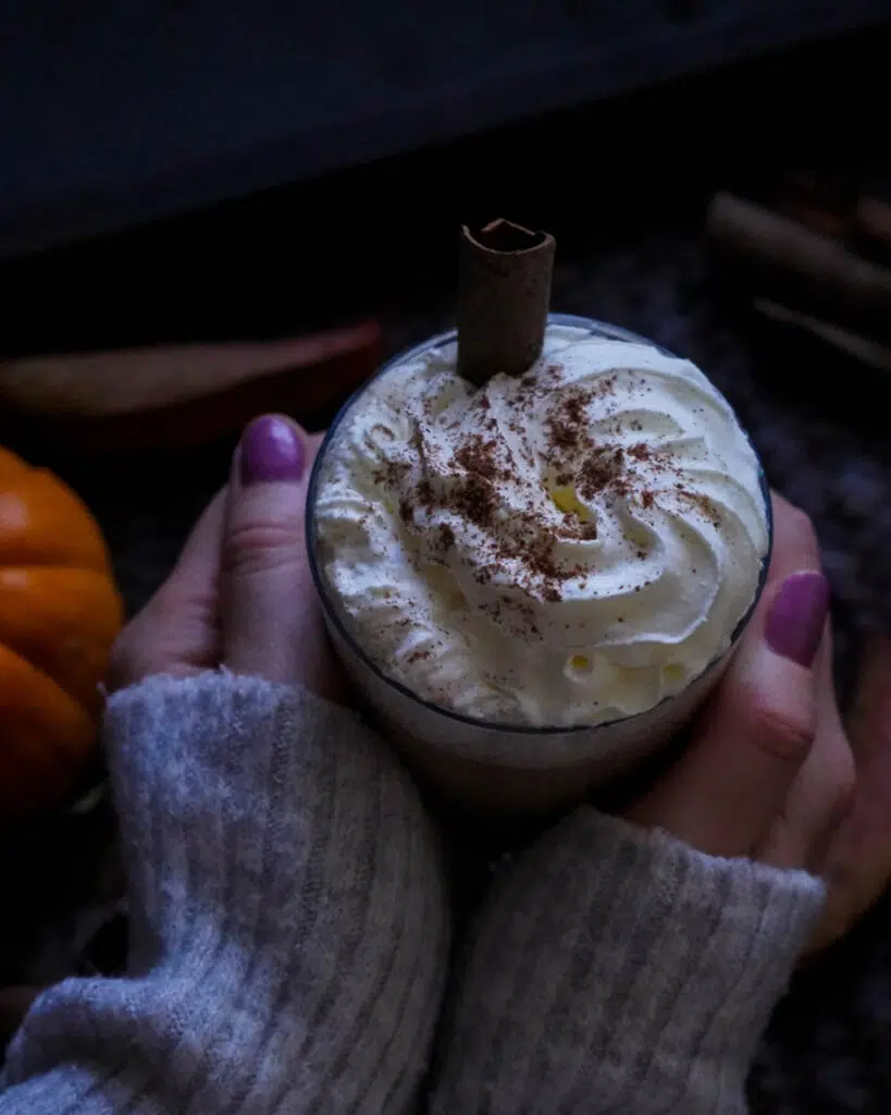 A warming mug of vegan pumpkin spice latte with hands cupped around it