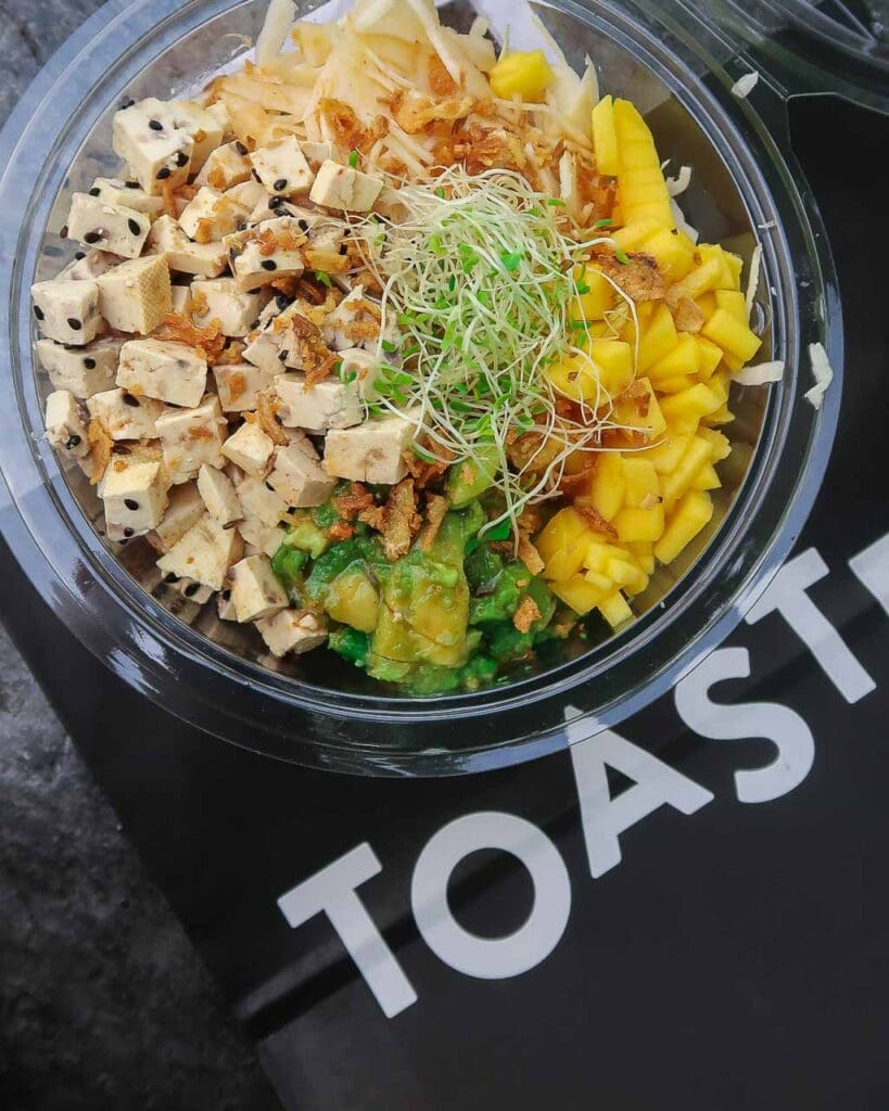 A takeaway dish of quinoa, mango, avocado, marinated tofu and garnish